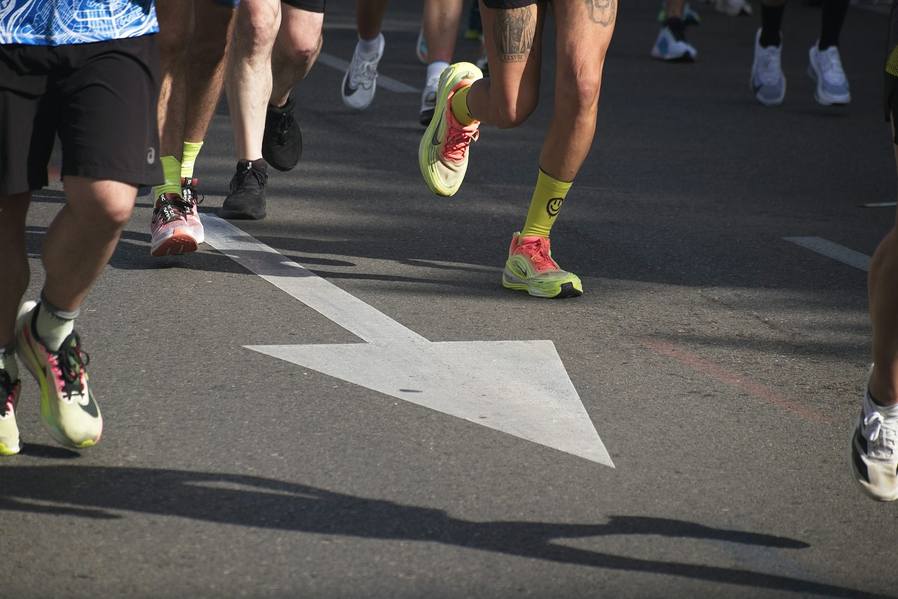 Grupo de corredores en una carrera urbana, frente a una flecha blanca en el pavimento.